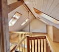 An attic space with wooden beams, exposed wooden ceiling, skylights, and a wooden staircase leading to a lower level.