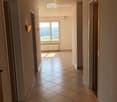 Empty hallway with tiled floor, beige walls, and a large window at the end showing a scenic view. The ceiling has recessed lighting and a wooden panel design.