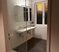 Modern bathroom with double sink, mirrored cabinet, glass-enclosed shower, and frosted windows.