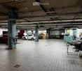 Garage with tiled floor, fluorescent lighting, two cars (one with hood open), tool cabinets, and workbenches.