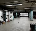 Garage with tiled floor, white brick walls, fluorescent lighting, and several parked cars. Cleaning tools and supplies are visible along the walls.