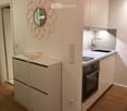 Modern kitchen with white cabinets, a sink, a faucet, an oven, a decorative mirror, and a bowl on the counter.
