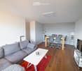 Open-plan living and dining area with a grey sectional sofa, white coffee table, dining table with chairs, and a TV stand with a flat-screen TV.