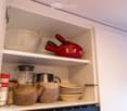 Open kitchen cabinet with neatly organized kitchenware including bowls, teapots, cups, a blender, canned goods, and plates.