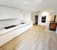 Modern kitchen with white cabinets, wooden flooring, and built-in appliances including a sink, faucet, and oven.