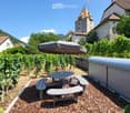 Outdoor seating area with a table, benches, and an umbrella, surrounded by vineyards and a stone wall, with a historic castle in the background.