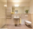 Modern bathroom with a white sink, toilet, large mirror, towel, and a glass-enclosed shower area.