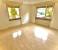 Empty room with light wooden flooring, white walls, and large windows with wooden sills. Radiator visible under one window.
