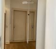A narrow hallway with wooden flooring, white walls, and a closed door at the end. A large mirrored cabinet is visible on the right side.