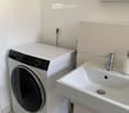 Bathroom with a white washing machine, a white sink with a silver faucet, and a bottle on the sink.
