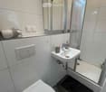 Modern bathroom with white tiles, a toilet, a sink with a mirror above it, and a shower area with a glass door.