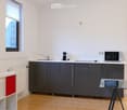 Modern kitchen with grey cabinets, white countertops, a sink, a coffee maker, a microwave, and a glass table.