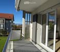 Balcony with glass doors, metal railing, and view of a grassy area and neighboring building.