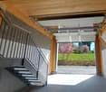 Open garage door, metal handrail, concrete floor, wooden ceiling, view of a grassy field