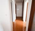 A long hallway with a brown tiled floor and white walls. It leads to an open doorway.