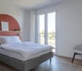 bedroom with bed, white sheets, white pillows, chair, glass doors, lamps, framed artworks, floored with wood