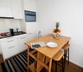 modern kitchen, wooden table, white cabinets, microwave, sink, dish cabinet, coffee maker, plate on table, bowl of fruits, plate on counter