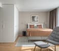 double bed with pillows, rug, chair, nightstand, lamps, beige wall, picture frame, window, white ceiling