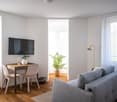 small room with a desk, two chairs, a couch, a TV, a lamp, and a potted plant