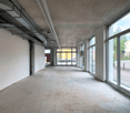 Empty corridor, concrete floor, white walls, ceiling with pipes, multiple glass windows, view of parking lot
