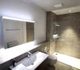 modern bathroom with white sink, mirror, toilet, shower, and tiled walls
