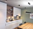 modern kitchen with white cabinets, wooden dining table, black chairs, sink, faucet, countertop, shelves, picture frame, lamps