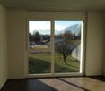 Spacious room with large windows overlooking a scenic outdoor landscape. The room has a tiled floor and neutral-colored walls, providing a clean and minimalist aesthetic. The view through the windows showcases a grassy area with a tree and distant mountai