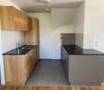 Modern kitchen with wooden cabinets, black countertops, built-in dishwasher, and gray tile flooring.