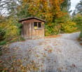 small wooden storage shed, gravel driveway, autumn foliage, stone wall