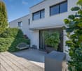 Modern white house, large windows, entrance with bench, potted plants, paved walkway