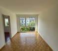 Spacious room with large windows overlooking a balcony or terrace, hardwood parquet flooring, and white walls.