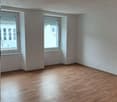 Empty room with wooden floor, two windows, and white walls.