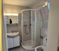 Bathroom with tiled flooring, shower, toilet, sink, mirror, cabinet, and a window