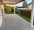 covered patio with tile floor, metal grill drain, garden, hedge, distant mountains