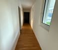 Empty corridor with wooden floor, white walls, doors, and windows