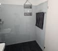 Tiled bathroom with gray walls, black floor tiles, shower, towel rack, and a hanging storage unit.