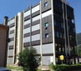 A multi-story office building with a modern, geometric facade made of glass and metal panels. The building has several floors and appears to be located in an urban setting with landscaping and parking spaces around it.