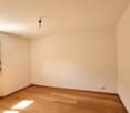 Empty room with wooden floor, radiator, window, and power outlet.