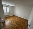 Empty room with wooden floor, white walls, large window, wall heater, ceiling lamp