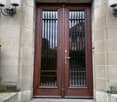 front entrance to a building, large wooden double doors with glass panes and metal grilles, two lanterns, concrete steps