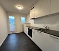 modern kitchen, stainless steel appliances, white cabinetry, black countertops, balcony, large windows