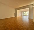 Spacious room with wooden parquet flooring, sliding glass doors leading to a balcony, white walls and ceiling, radiator, open door to another room