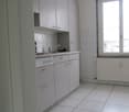 White cabinets, tiled floor, stainless steel sink, window, electrical outlet.