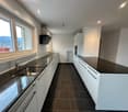 Open kitchen, black granite countertops, white cabinets, stainless steel sink, windows, tiled floor