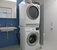 modern white washer and dryer, sink, mirror, blue wall, white tiled floor