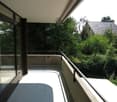 Concrete balcony with glass door, metal railing, paved floor, view of greenery