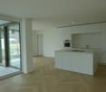 Modern interior, white kitchen, built-in appliances, wooden floor, glass doors to balcony