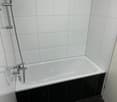 Modern bathroom with white tiles, a white bathtub, and a silver shower head.