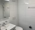 Modern bathroom with white tiles, a white sink, a toilet, and a mirror with a light above it.