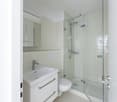 Square bathroom with white tiles, toilet, sink, mirror, and shower enclosure